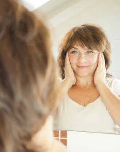 older woman looking in mirror touching face
